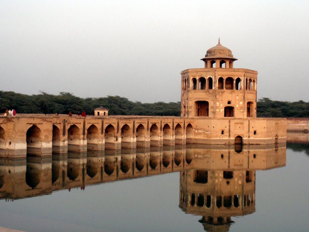 Hiran Minar monument with arched bridge and reflection in water surrounded by greenery