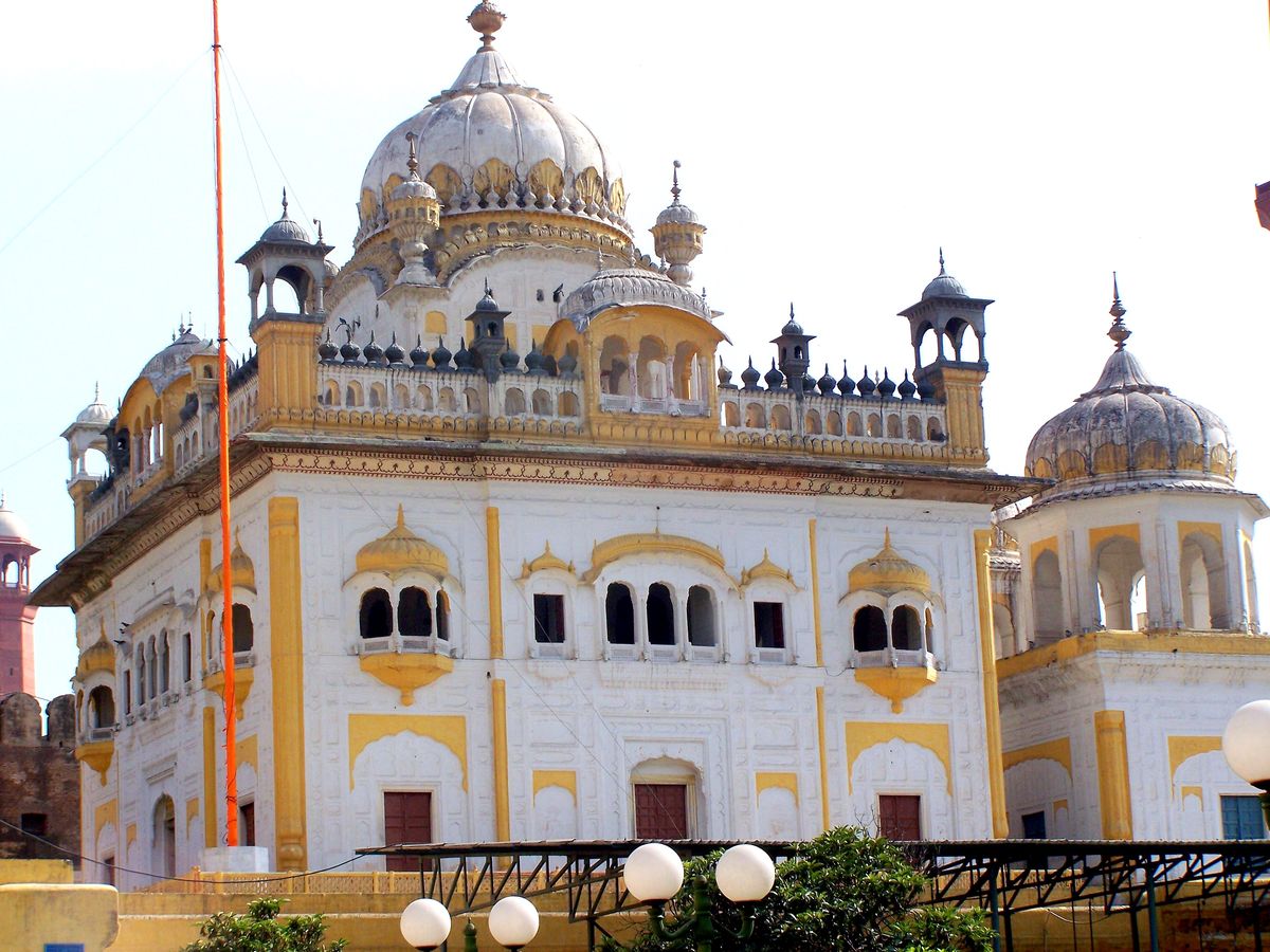 Sikh Gurdwara with white domes, yellow accents, jharokhas, and Nishan Sahib flagpole