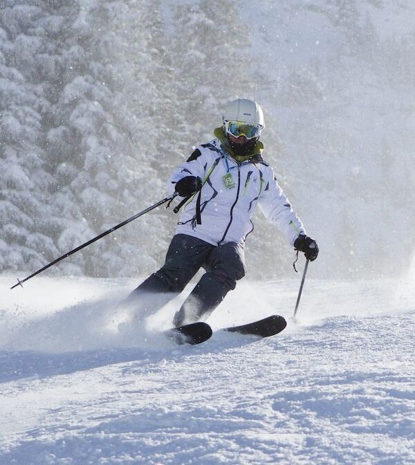 Skier mid-turn on snowy slope with snow spray and forest backdrop