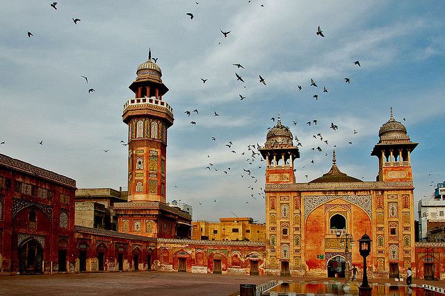Wazir Khan Mosque with colorful tilework, minarets, domes, and birds flying above courtyard