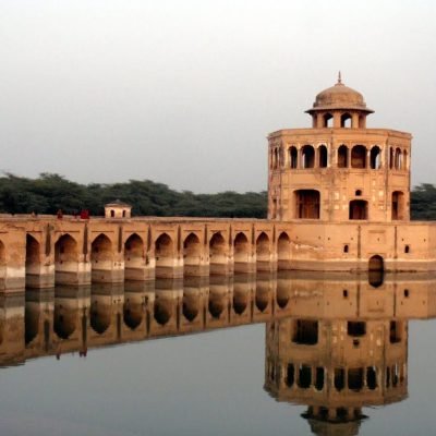 Hiran Minar monument with arched bridge and reflection in water surrounded by greenery