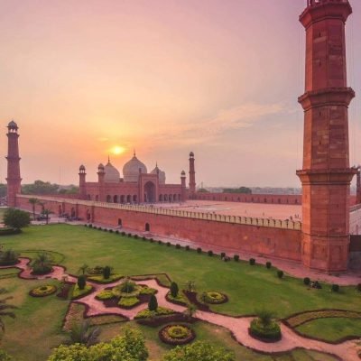 Badshahi Mosque at sunset with domes, minarets, and landscaped garden in foreground