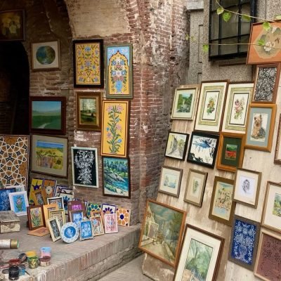 “Outdoor art display with framed paintings and supplies against rustic brick wall