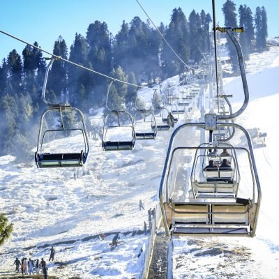 Ski lift ascending snowy mountain with people and evergreen trees below