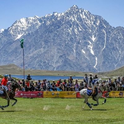 Chitral Polo players riding horses on a grassy field during a match.