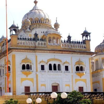 Sikh Gurdwara with white domes, yellow accents, jharokhas, and Nishan Sahib flagpole
