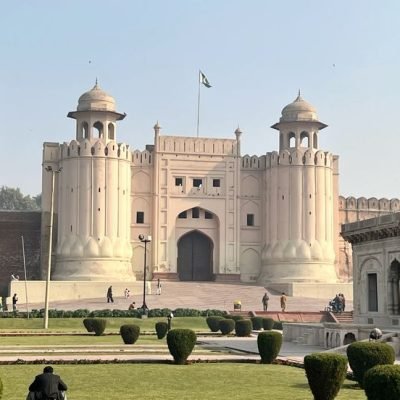 Lahore Fort entrance with cylindrical bastions, garden, Pakistani flag, and adjacent Mughal building