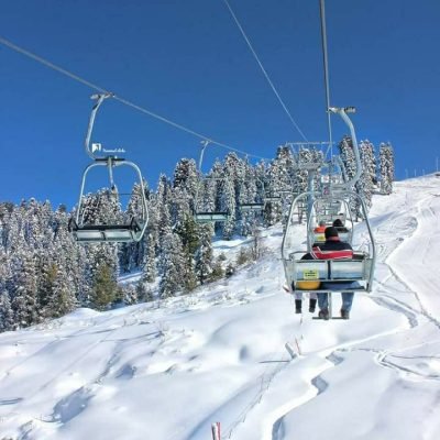 Ski lift ascending snowy mountain with people and evergreen trees below