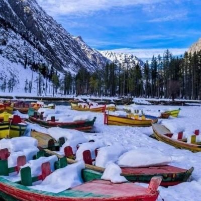 Snow-covered colorful boats near frozen lake with pine trees and mountains