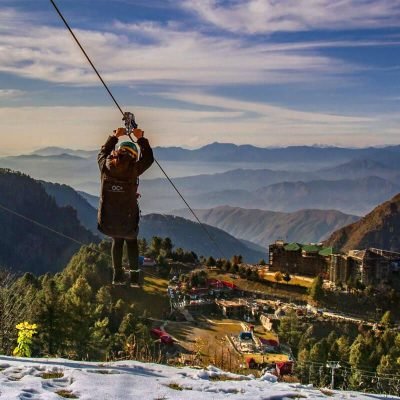 Person zip-lining over snowy mountain valley with town and ridges below
