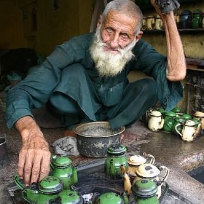 Elderly man arranging green teapots in a traditional tea shop
