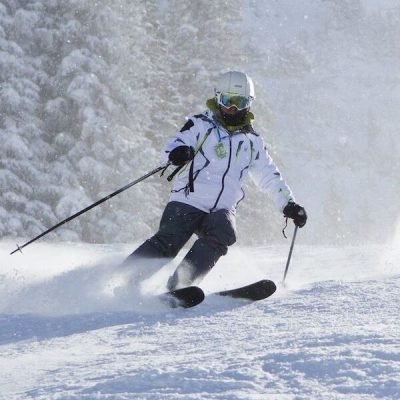 Skier mid-turn on snowy slope with snow spray and forest backdrop
