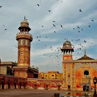 Wazir Khan Mosque with colorful tilework, minarets, domes, and birds flying above courtyard