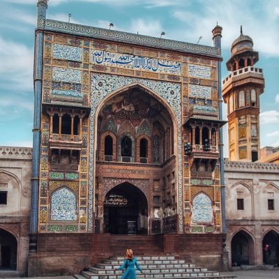 Entrance of Wazir Khan Mosque with colorful tilework, Arabic calligraphy, and woman in blue dress